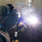 Soldador utilizando eletrodo revestido E6013 3.2X350MM para soldagem, demonstrando o uso do produto Tradestar em aplicações de serralheria e construção. Imagem ilustrativa do processo de solda com faíscas e fumaça.