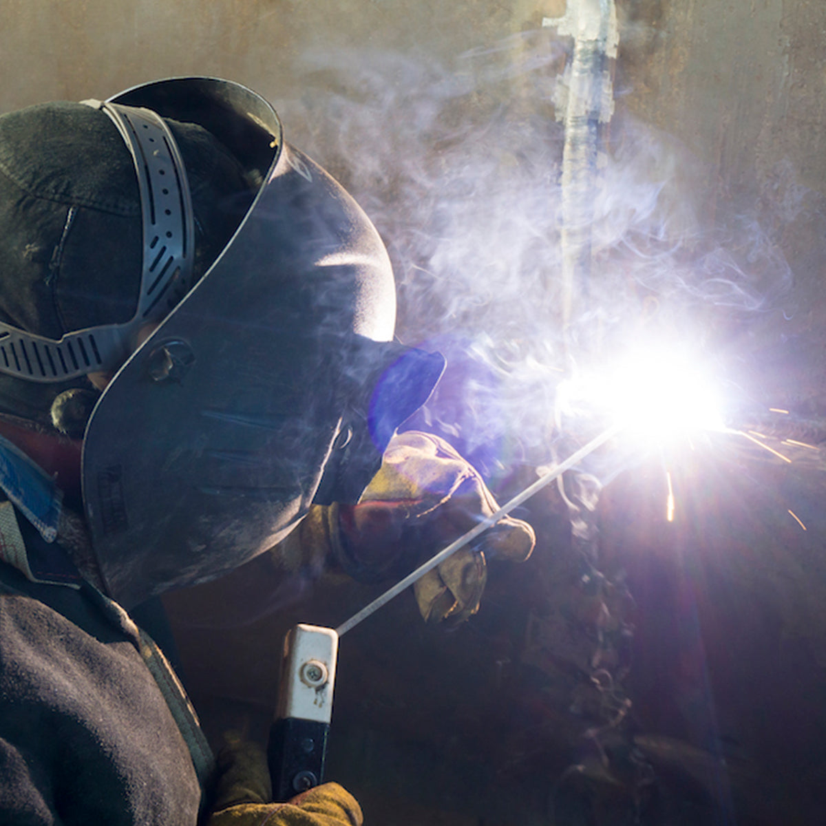 Soldador utilizando eletrodo revestido E6013 4.0mm Tradestar para soldagem, demonstrando o uso do produto em aplicações de serralheria e construção. Imagem ilustrativa da solda com faíscas e fumaça.
