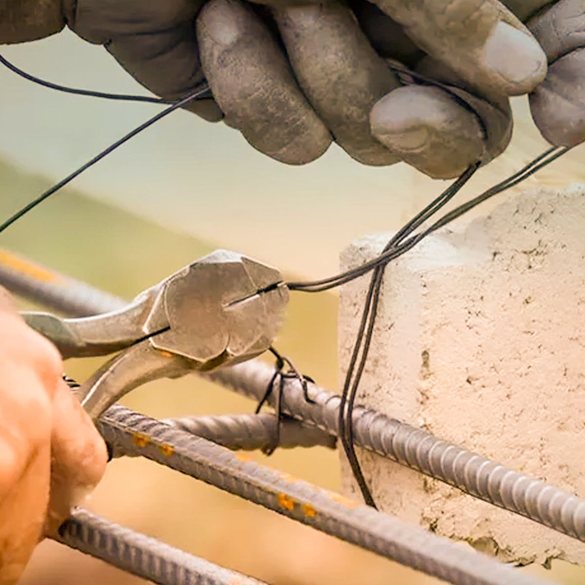 Kit Arame Recozido Liso 1 Kg e Alicate Torquês Armador em uso na construção civil, mostrando o arame sendo cortado para amarração de ferragens em concreto armado. Ferramentas e materiais para construção e reforço estrutural.