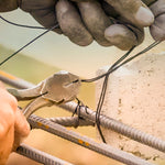 Kit Arame Recozido Liso 1 Kg e Alicate Torquês Armador em uso na construção civil, mostrando o arame sendo cortado para amarração de ferragens em concreto armado. Ferramentas e materiais para construção e reforço estrutural.