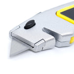 Kit 26 Estiletes Trapezoidal 18mm + Refil C/ 50 Peças - Estilete metálico com lâmina trapezoidal exposta, botão de trava preto e detalhes em amarelo. Ideal para cortes precisos em diversos materiais, com empunhadura emborrachada para conforto e segurança.