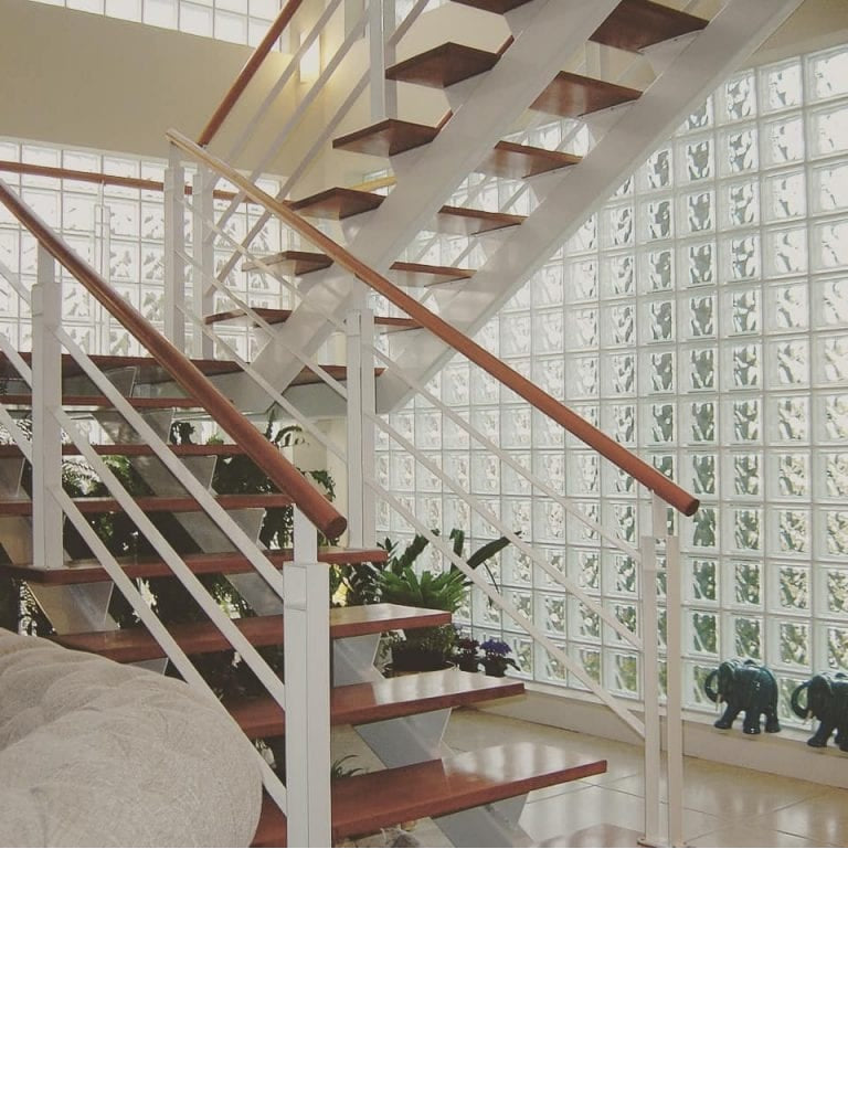 Escada moderna com corrimão branco e degraus de madeira, ao lado de uma parede de blocos de vidro estrelas Tradestar, proporcionando iluminação natural e design elegante. Kit com 6 tijolos de vidro para construção e decoração de ambientes internos e externos.