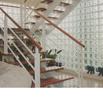 Escada moderna com corrimão branco e degraus de madeira, ao lado de uma parede de blocos de vidro estrelas Tradestar, proporcionando iluminação natural e design elegante. Kit com 6 tijolos de vidro para construção e decoração de ambientes internos e externos.